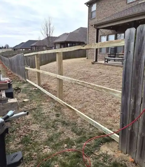 Old pine fence before replacement, with new rails set on the posts beside the weathered boards