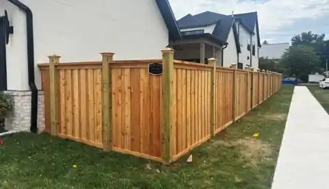 Cedar cap-and-trim privacy fence with tall capped posts along a new home's sidewalk in Bentonville