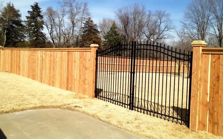 Cedar board-to-board fence with an arched black iron double gate hung between capped cedar columns