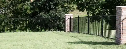 Black ornamental iron fence running between brick columns across an open lawn