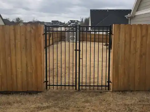 Black iron double gate set into a wood privacy fence