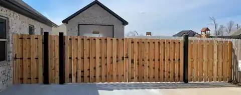 Shadow-box wood drive gates on black steel frames across a driveway in Elm Springs
