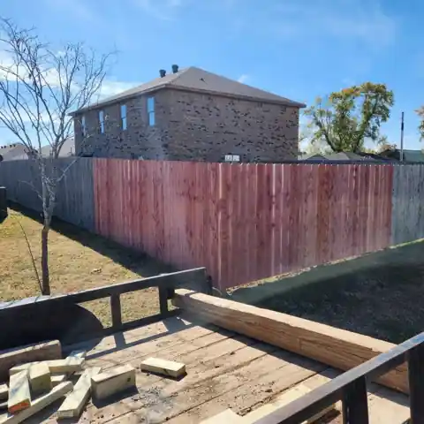 New cedar section replacing an old grey fence, seen from the crew trailer loaded with lumber